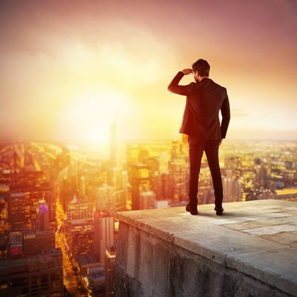 A man on a rooftop, above a city, looking out at the rising, or setting, sun.