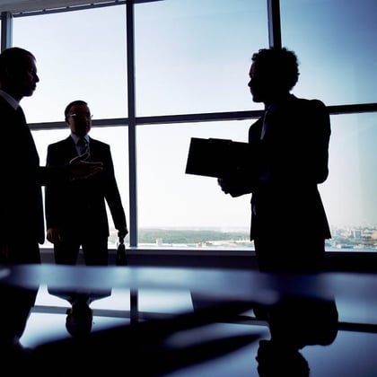 Executives silhouetted against the windows of a dark office.