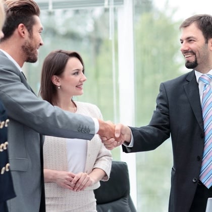 An advisor meeting with two clients and shaking hands with one