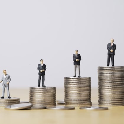 Figures of businessmen standing on coins signifying wealth gap