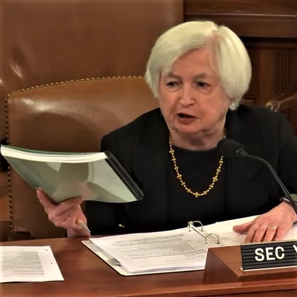 Treasury Secretary Janet Yellen holds up a big paperback book with a green cover.