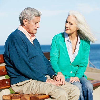 A man and a woman sit on a bench at the beach.