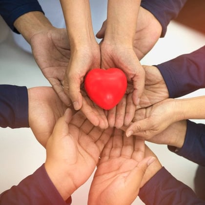 Hands of six people holding a small plastic heart