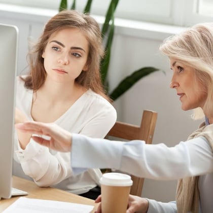 Two women using a computer and talking to each other.
