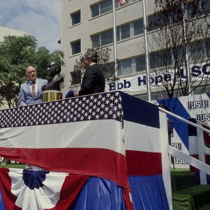 Bob Hope appears on a podium in front of a 10-story building that was completed in 1963.