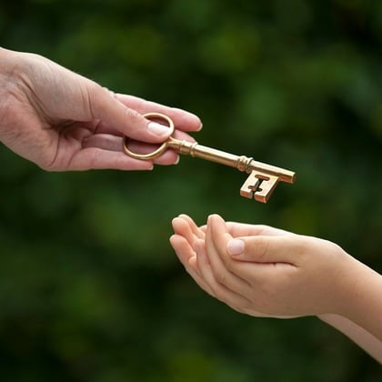 Hand passing key to child's hands symbolizing wealth transfer