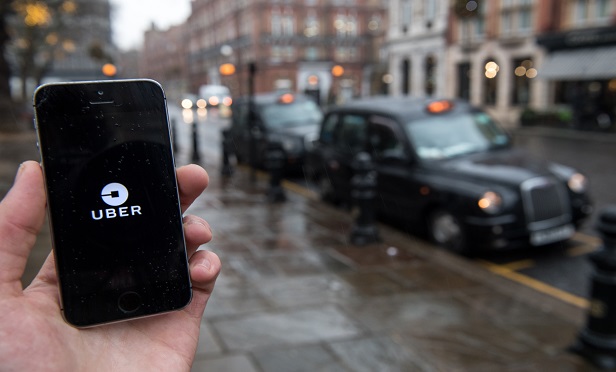 An Uber Technologies Inc. logo sits on a smartphone display in this arranged photograph as London taxis sit parked beyond in London, U.K., on Friday, Dec. 22, 2017. Uber will be regulated in European Union countries as a transport company after the bloc's top court rejected its claim to be a digital service provider, a decision that could increase legal risks for other gig-economy companies including Airbnb. Photographer: Chris J. Ratcliffe/Bloomberg